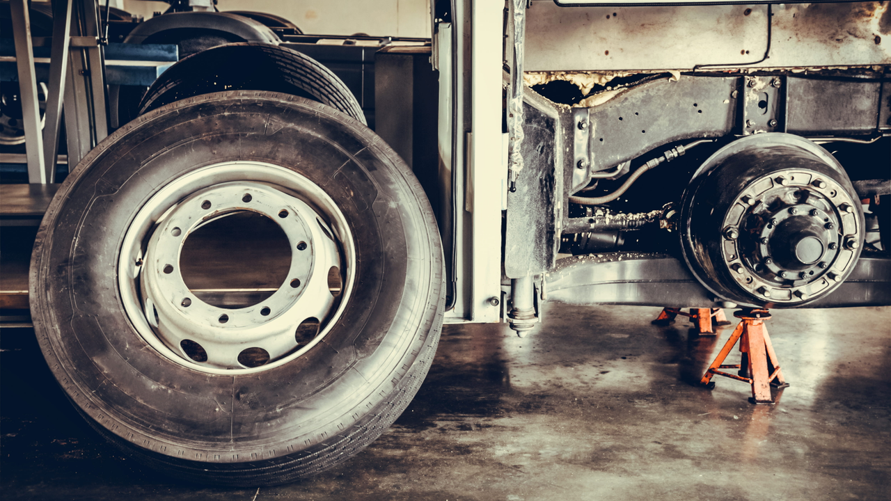 A bus wheel resting against a chassis with a workshop in the background.